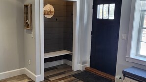 Quarto com piso de madeira em padrão espinha de peixe, porta azul escura e porta branca que dá para um armário com prateleiras.