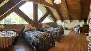 Un dormitorio abrigado en el ático con dos camas, una mesa con un tablero de ajedrez y ventanas amplias.