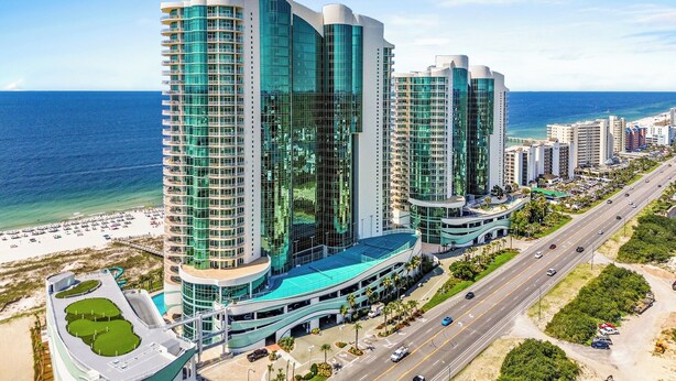 A modern hotel with multiple high-rise buildings, a beachfront, and a road with vehicles.