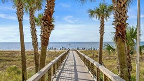 A wooden boardwalk leading to a beach with palm trees and beach umbrellas.