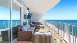 A balcony with wicker furniture, a hot tub, and a TV screen.
