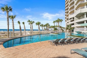 A swimming pool with lounge chairs, palm trees, and a view of the ocean.