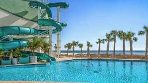 A swimming pool with multiple slides, palm trees, and a view of the ocean.