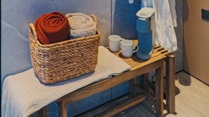 A bathroom with a towel rack, a basket of towels, a coffee maker, and a small table.