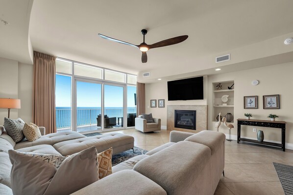 A spacious living room with a large sofa set, a ceiling fan, a fireplace, and a view of the ocean. - Beach Luxury ~ Turquoise C1805 Balcony HotTub & TV (Orange Beach)