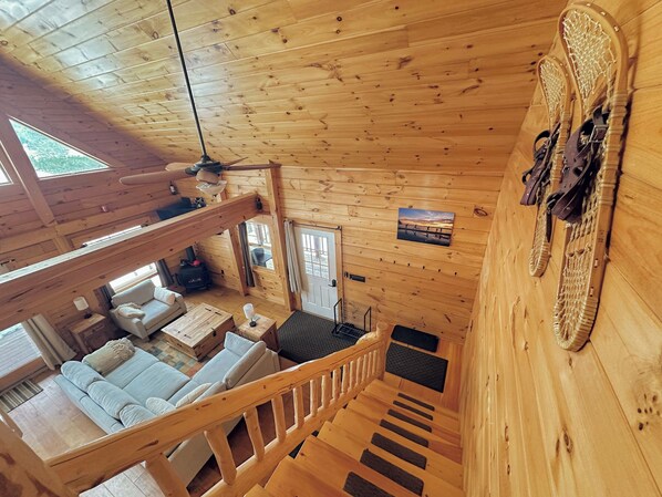 Interior de una cabaña de madera con habitación en el entrepiso, comedor y sala de estar con sofá y chimenea.