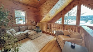Interior acogedor de una cabaña con techo de madera, ventilador de techo, sofá modular, una mesita y vistas del paisaje nevado.