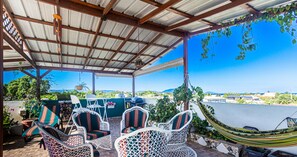 A covered outdoor seating area with wicker chairs and a hammock, overlooking a scenic landscape.