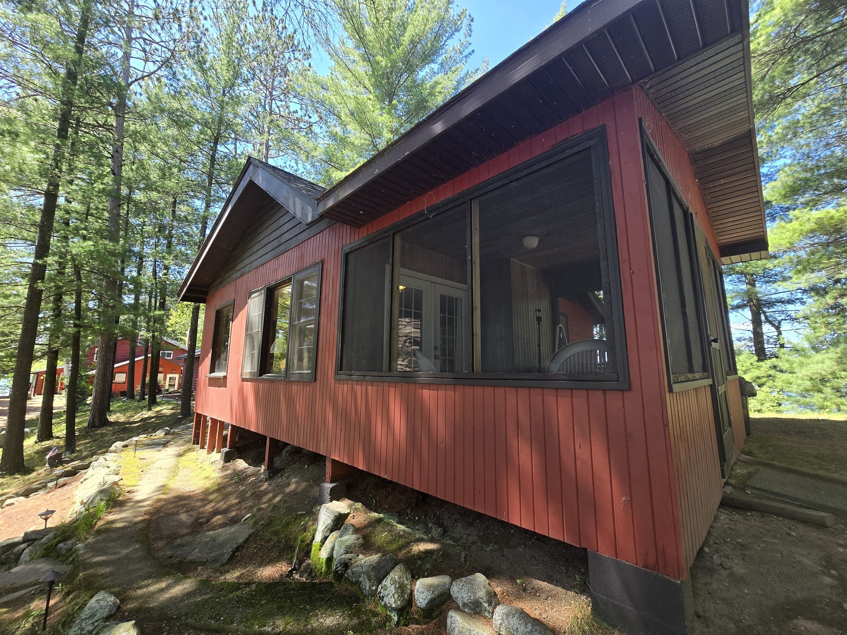 A red cabin with large windows, surrounded by trees and a stone pathway.