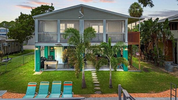 Une maison à deux étages dotée d’un porche abrité, d’un petit espace extérieur aménagé avec des chaises et d’une terrasse autour de la piscine.
