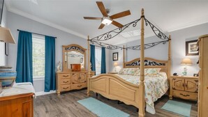 Un lit à baldaquin avec une tête de lit en bois, un ventilateur de plafond et un grand miroir placé au-dessus.
