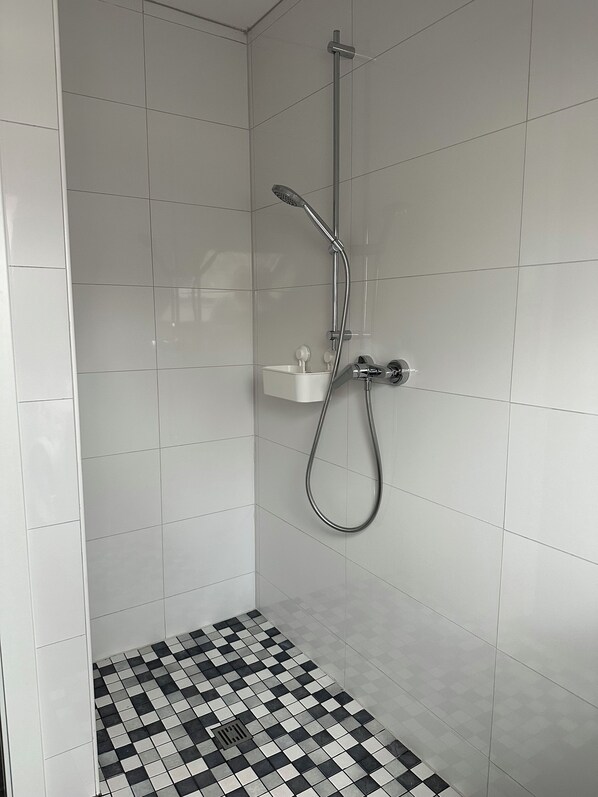 A shower with a handheld showerhead and a wall-mounted faucet.