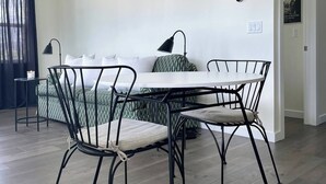 Et moderne spiseområde med et hvidt bord, sorte metalstole og en stor hængende lampe.