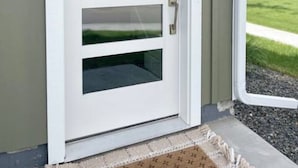 En hvid dør med et glasfelt og en dørhåndtag, placeret i en lys farvet facade.