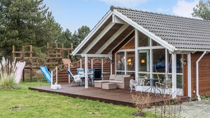 A wooden house with a sloped roof, a covered patio with outdoor furniture, and a wooden deck. - Awesome home in Rødby with sauna (Rødby)