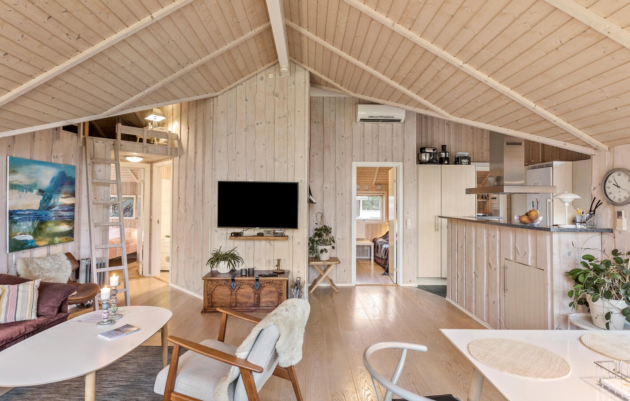A spacious living area with wooden walls, a mounted TV, and a kitchen area with cabinets and a clock.