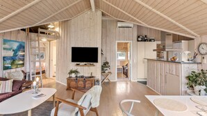 A spacious living area with wooden walls, a mounted TV, and a kitchen area with cabinets and a clock. - Awesome home in Rødby with sauna (Rødby)