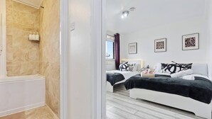 A modern hotel room with a shower area, two beds, and artwork on the walls.