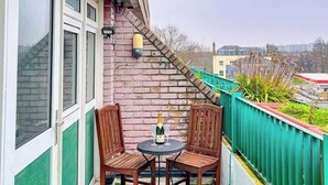 A balcony with two wooden chairs, a small round table, and a bottle of champagne.