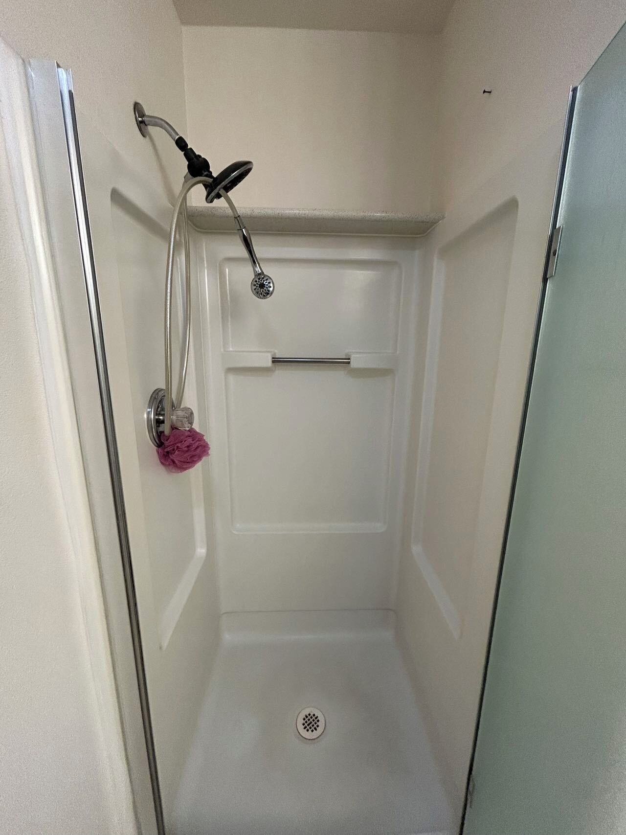 A small, enclosed shower stall with a handheld showerhead, a towel rack, and a drain.