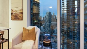Una sala de estar moderna con un amplio ventanal que da a un paisaje urbano, un sillón cómodo y un objeto decorativo sobre una mesita.