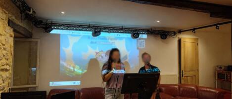 A room with a stone wall, a wooden ceiling, a red leather couch, a wooden table with a laptop, and a projection screen displaying a cartoon character.