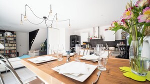 Un espace de salle à manger moderne avec une table en bois dressée pour quatre personnes, un lustre et un vase rempli de fleurs.
