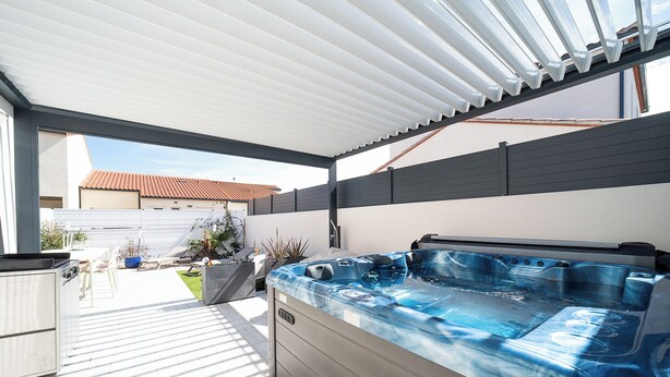 Un espace extérieur abrité comprenant un jacuzzi, un barbecue et une terrasse avec des chaises et des plantes.