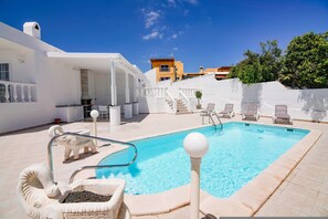Una piscina con revestimiento blanco, una escalera de piedra y sillas de descanso.