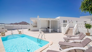 Zona de piscina en la azotea con sillones, una escalera de piscina y una escalera que lleva a un nivel superior.