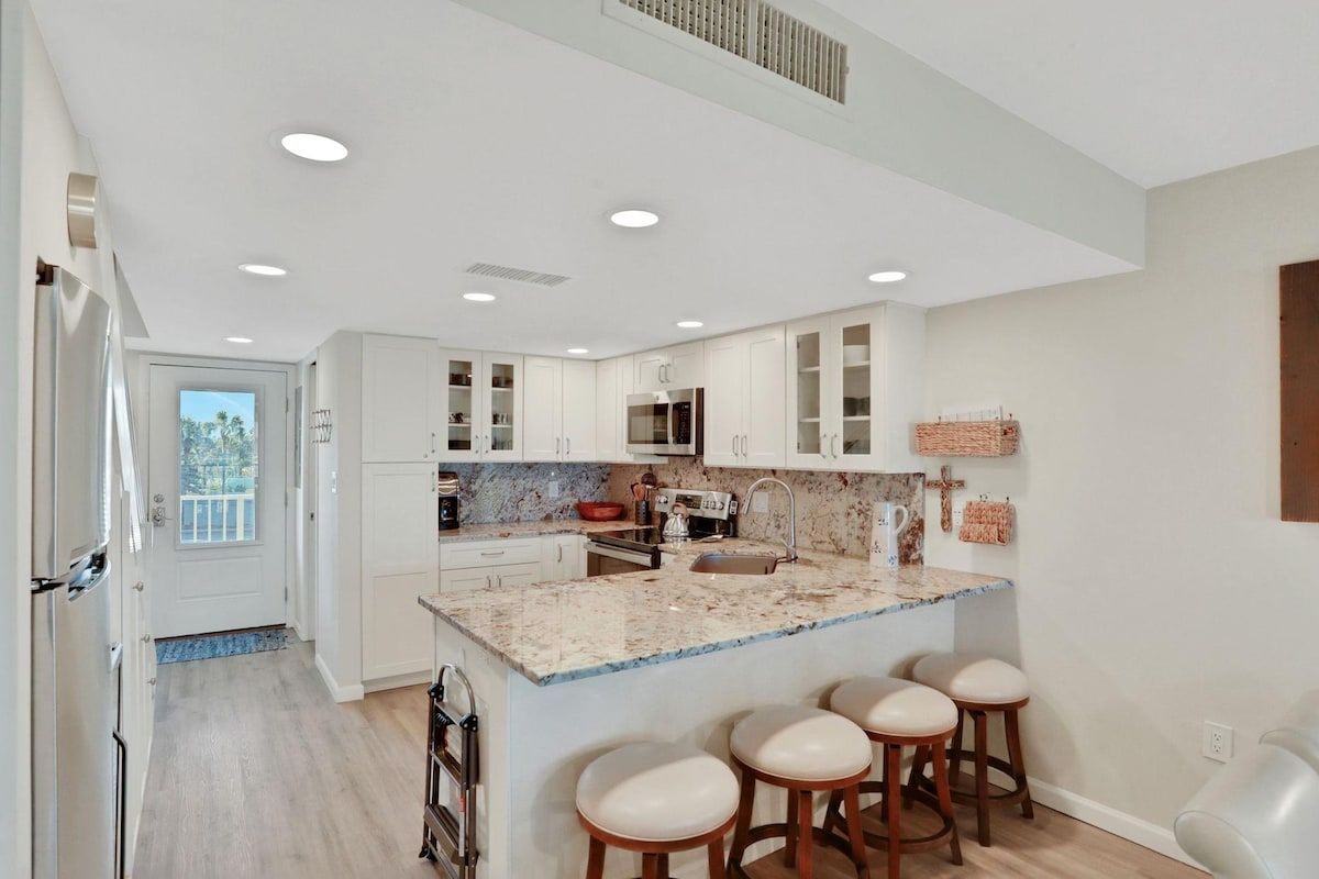 Una cocina moderna con armarios blancos, encimera de granito y una isla central con taburetes de bar.
