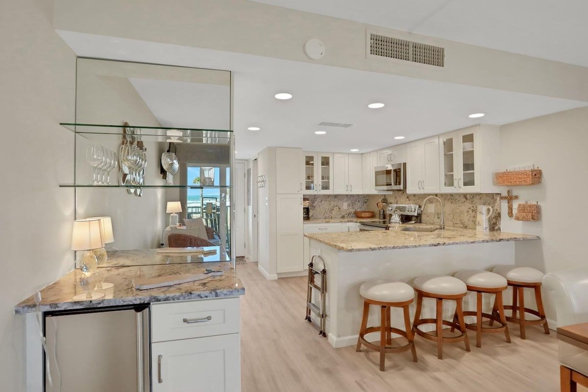 A modern kitchen with a marble countertop, white cabinets, and a central island with bar stools.