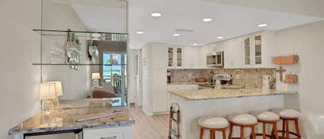 A modern kitchen with a marble countertop, white cabinets, and a central island with bar stools.