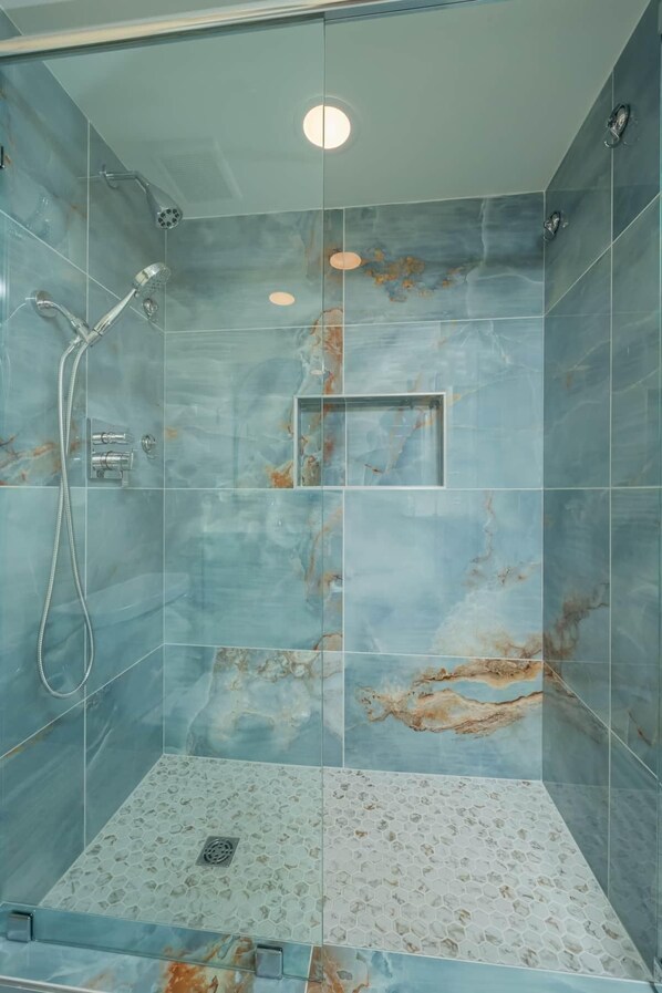 A glass-enclosed shower with a marble-like tile design and a built-in rectangular mirror.