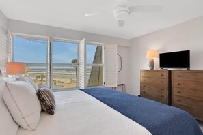 A bedroom with a bed, a TV, a dresser, and a window with a view of the beach.