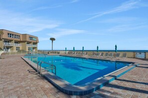 A swimming pool with a clear view of the ocean, surrounded by lounge chairs and a building with balconies.