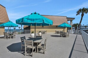 An outdoor patio area with tables and chairs, blue umbrellas, and a view of the ocean.