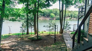 A lakeside deck with a stone pathway leading to a dock, surrounded by trees and a view of the lake. - Peaceful Retreat on the Lake (Hot Springs Village)