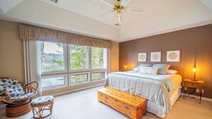 A bedroom with a large bed, a wooden bench, a wicker chair, and a ceiling fan. - Peaceful Retreat on the Lake (Hot Springs Village)