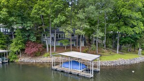 A docked boat with a covered seating area, surrounded by trees and a house in the background. - Peaceful Retreat on the Lake (Hot Springs Village)