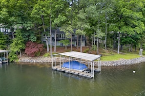 A docked boat with a covered seating area, surrounded by trees and a house in the background.