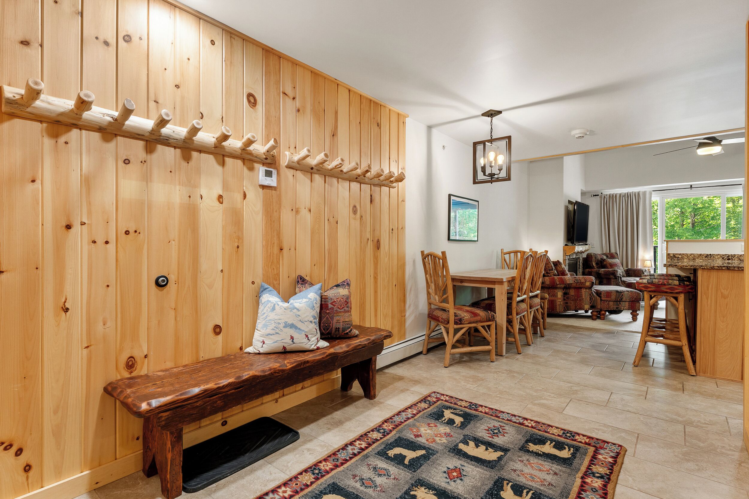 A wooden interior with a bench, chairs, a rug, and a wooden wall with hooks.