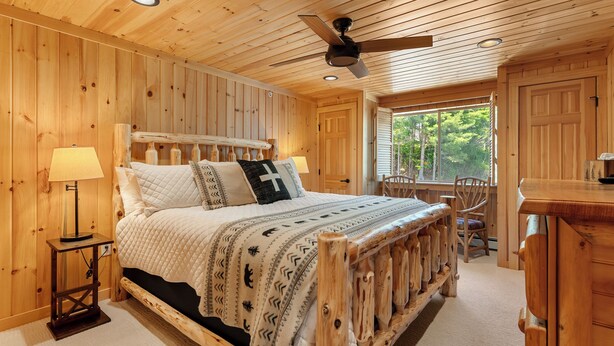 Une chambre dans une cabane en bois, avec un lit, une table de chevet, un bureau et une fenêtre.
