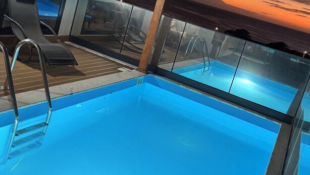 An indoor swimming pool with clear blue water, surrounded by lounge chairs and a glass barrier. - Apartment with swimming pool and magnificent view of Tarrafal Bay (Tarrafal)