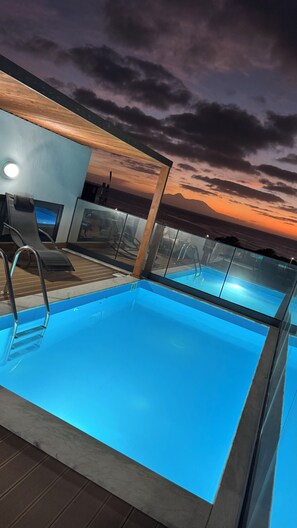 Une piscine intérieure à l’eau d’un bleu cristallin, entourée de chaises longues et séparée du reste de l’espace par une paroi de verre.