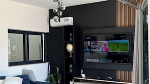 A modern living room with a blue sofa, a glass coffee table, a flat-screen TV, and a wooden accent wall. - Apartment with swimming pool and magnificent view of Tarrafal Bay (Tarrafal)