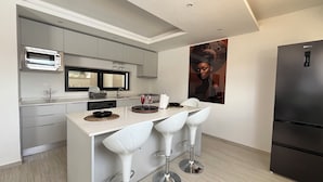 A modern kitchen with a built-in microwave, a refrigerator, and a dining area with white bar stools. - Apartment with swimming pool and magnificent view of Tarrafal Bay (Tarrafal)