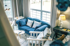 Un salon avec un canapé bleu, un fauteuil blanc, une petite table et une lampe.