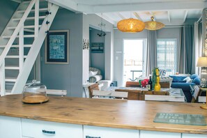 Une cuisine moderne avec un plan de travail en bois, une table basse en verre et un escalier doté d’une rampe blanche.