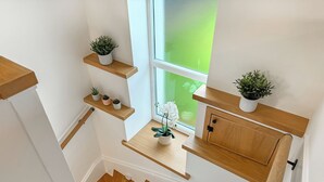 Een trap met houten treden en witte muren, met ingebouwde planken met potplanten en een raam met uitzicht op groen.